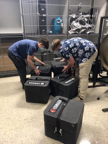 Two drumline members put snare drum cases away in the storage room 