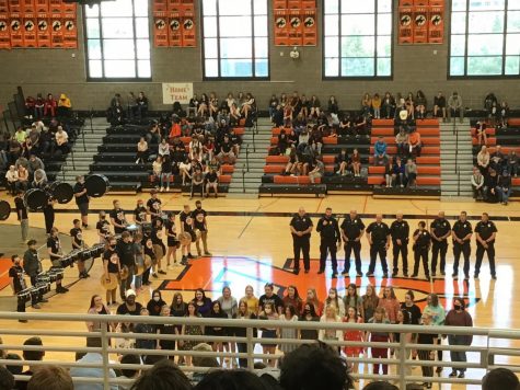 police officers stand in a line surrounded by orang and black decorations in a high school gym.