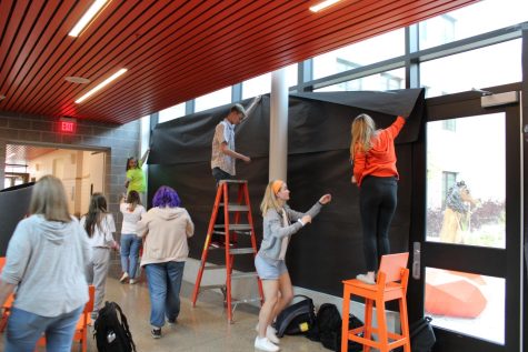 Students in orange and grey hoodies hang black paper over windows.