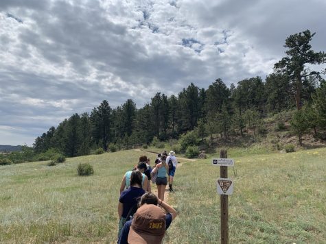 Students hike in a meadow with clouds in medicine bow.