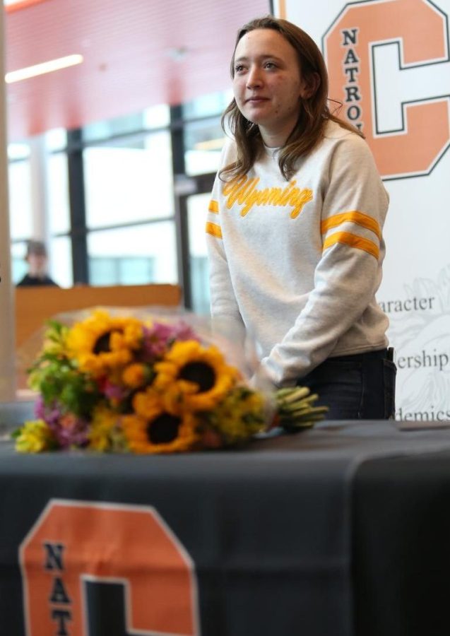 Baedke, wearing white and gold UW hoodie, flowers on table in front of her, NC poster behind.