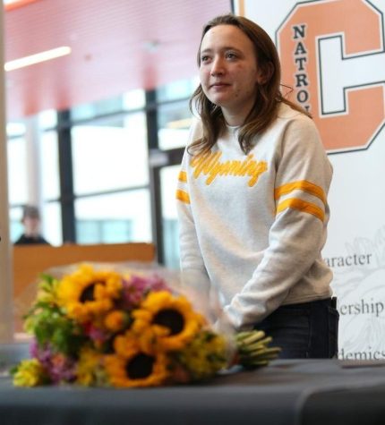 Baedke, wearing white and gold UW hoodie, flowers on table in front of her, NC poster behind.
