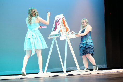 Girls in blue dresses fling paint on stage.