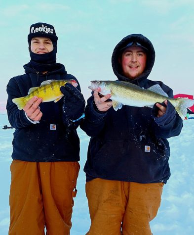 Two anglers standing on ice with perch and walleye.