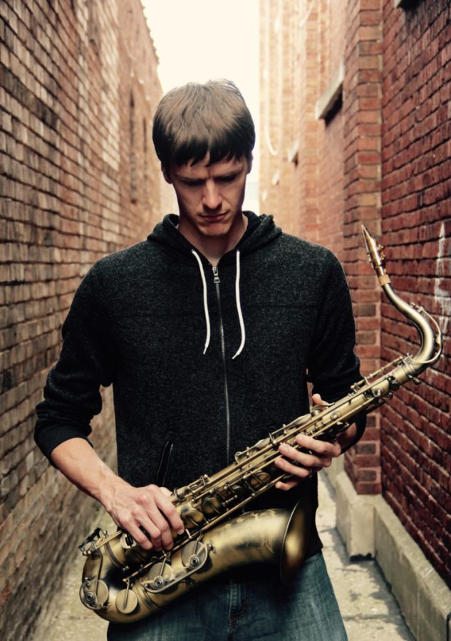 Musician with saxophone standing by brick wall.